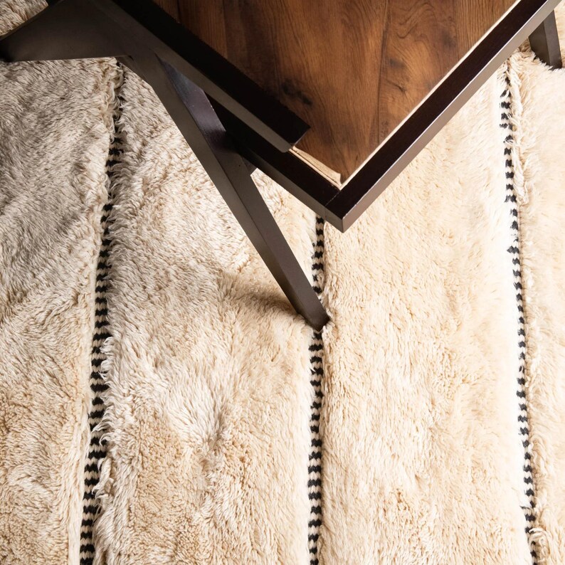 Beautiful handmade Moroccan rug in beige and black, featuring a bold geometric diamond pattern. Crafted from soft wool, it adds warmth and style to living rooms, bedrooms, or boho-chic spaces. Unique fringes enhance its artisan charm and timeless