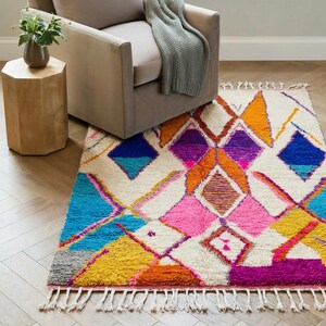 Authentic handmade Moroccan Boujaad rug featuring bold geometric diamond patterns in vibrant multicolor — electric blue, fuchsia pink, orange, yellow and purple on ivory wool background. Hand-knotted by Berber artisans in Morocco using natural wool. Perfect boho statement rug for living room, bedroom or dining room. One-of-a-kind colorful area rug with traditional fringe.