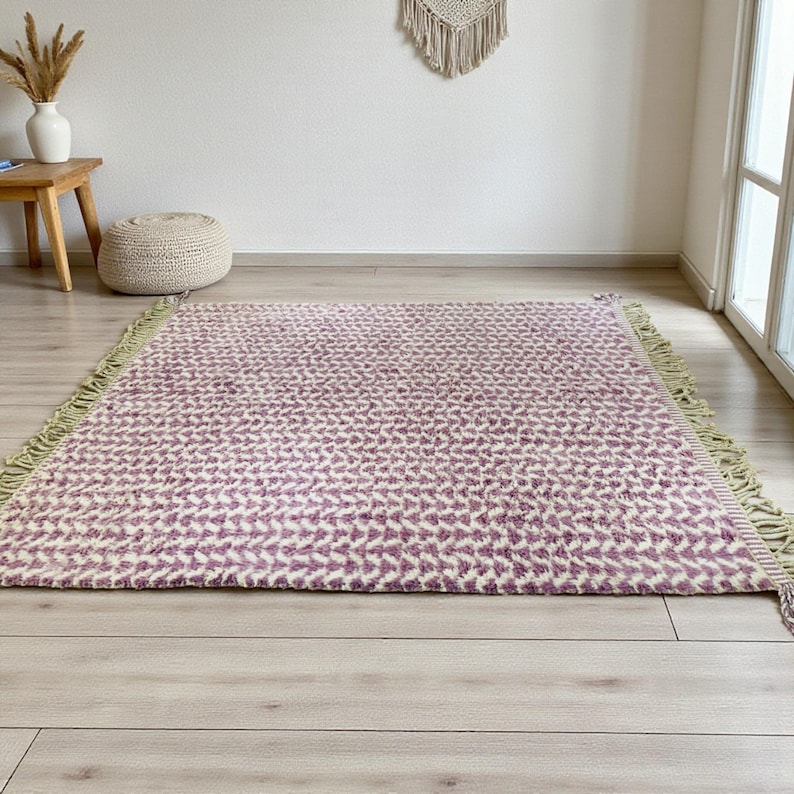 Handwoven Moroccan wool rug in wistful mauve and cream tones. Features a soft geometric pattern with textured pile and hand-knotted fringes. Perfect for living rooms, bedrooms, or boho interiors. Made from 100% natural wool by Berber artisans in Morocco. This handmade rug adds warmth, elegance, and Moroccan authenticity to modern or vintage-style spaces.