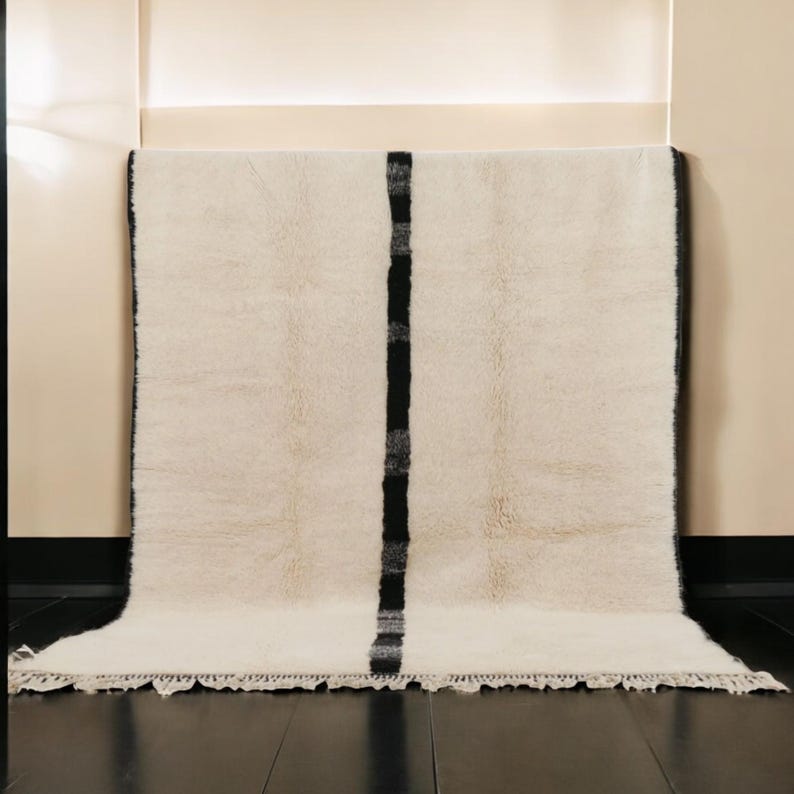 Handmade Moroccan wool rug featuring a minimalist black and white design. Ethically crafted by Berber artisans in Morocco using 100% natural wool. Thick, plush, and ultra-soft, this Beni Ourain-style carpet is perfect for modern, Scandinavian, and bohemian interiors. Ideal for living rooms, bedrooms, and luxury home decor. Available in custom sizes. Authentic tribal craftsmanship with eco-friendly materials. Free worldwide shipping with FedEx Express.