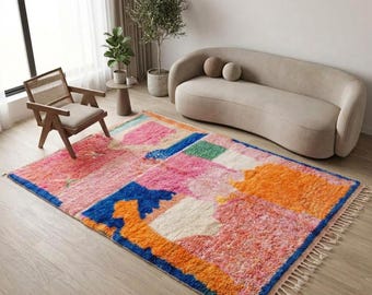 Può includere: Un tappeto rettangolare a pelo lungo con un vivace motivo geometrico astratto. Il design incorpora audaci blocchi di colore rosa, arancione, blu, verde e crema, rifinito con frange decorative lungo i bordi più corti.