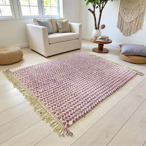 Handwoven Moroccan wool rug in wistful mauve and cream tones. Features a soft geometric pattern with textured pile and hand-knotted fringes. Perfect for living rooms, bedrooms, or boho interiors. Made from 100% natural wool by Berber artisans in Morocco. This handmade rug adds warmth, elegance, and Moroccan authenticity to modern or vintage-style spaces.
