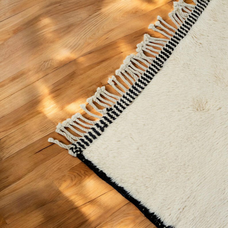 Handmade Moroccan wool rug featuring a minimalist black and white design. Ethically crafted by Berber artisans in Morocco using 100% natural wool. Thick, plush, and ultra-soft, this Beni Ourain-style carpet is perfect for modern, Scandinavian, and bohemian interiors. Ideal for living rooms, bedrooms, and luxury home decor. Available in custom sizes. Authentic tribal craftsmanship with eco-friendly materials. Free worldwide shipping with FedEx Express.