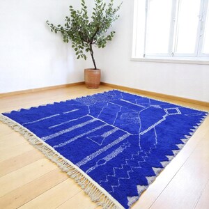 Striking handmade Moroccan rug in bold cobalt blue with white tribal Amazigh symbols. Crafted from natural wool, this unique Berber rug features traditional abstract lines and diamond motifs, perfect for adding a splash of color and culture to modern interiors. Ideal for boho, eclectic, or contemporary homes looking for a statement piece. Soft texture and timeless authenticity.