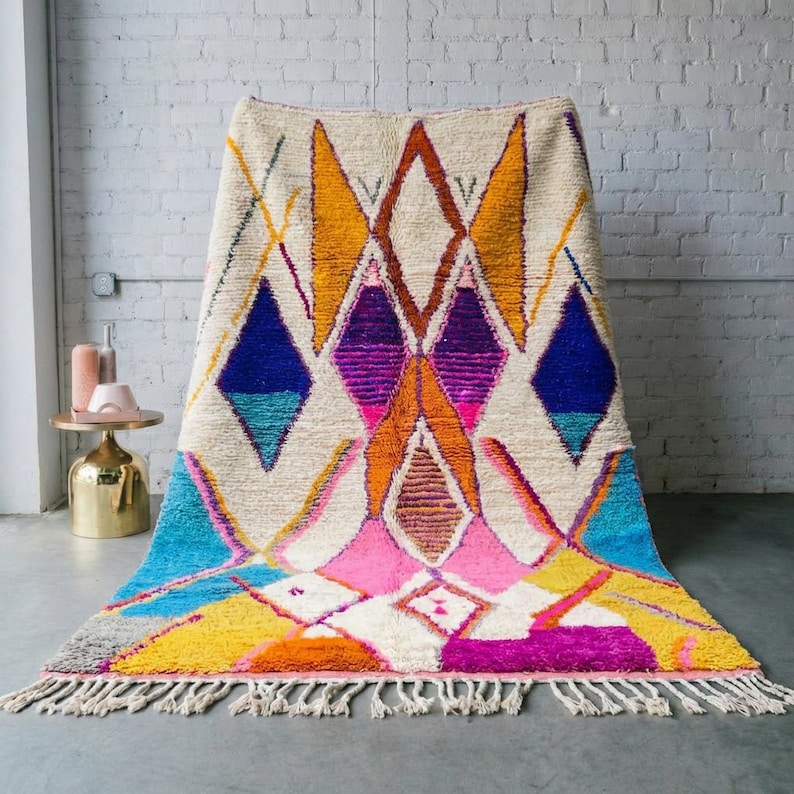 Authentic handmade Moroccan Boujaad rug featuring bold geometric diamond patterns in vibrant multicolor — electric blue, fuchsia pink, orange, yellow and purple on ivory wool background. Hand-knotted by Berber artisans in Morocco using natural wool. Perfect boho statement rug for living room, bedroom or dining room. One-of-a-kind colorful area rug with traditional fringe.