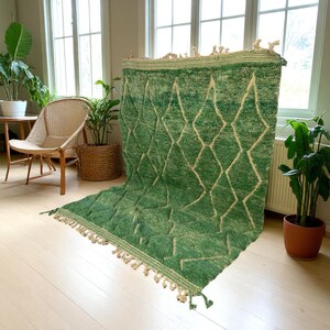 Green Moroccan wool rug with cream diamond lattice pattern, handmade in Beni Ourain style. Styled in a bright modern boho room with plants, rattan furniture, and natural light. The rug has a plush texture, tribal design, and fringe details, making it perfect for earthy, creative, or minimalist interiors. Crafted by Berber artisans, it's soft, thick, and ethically made using traditional weaving techniques.