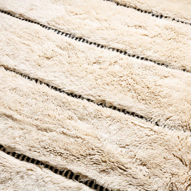 Beautiful handmade Moroccan rug in beige and black, featuring a bold geometric diamond pattern. Crafted from soft wool, it adds warmth and style to living rooms, bedrooms, or boho-chic spaces. Unique fringes enhance its artisan charm and timeless