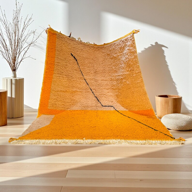 Handmade Moroccan rug in vibrant orange and soft beige with a bold abstract line design. Crafted by Berber artisans using pure wool, this rug combines traditional weaving with a modern artistic touch. Its warm, energetic tones make it a standout for living rooms, creative interiors, or bohemian spaces. Durable, eco-friendly, and soft underfoot, this orange and beige Berber wool carpet adds Moroccan charm and contemporary elegance to any home decor.