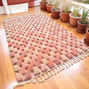 May include: A pink and cream shag rug with a geometric pattern. The rug has a fringe border.