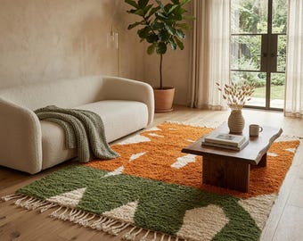 Può includere: Un tappeto rettangolare a pelo lungo con un motivo geometrico nei toni dell'arancione bruciato, verde oliva e crema. Il tappeto è rifinito con frange color crema lungo i bordi più corti, creando una superficie tattile sul pavimento.
