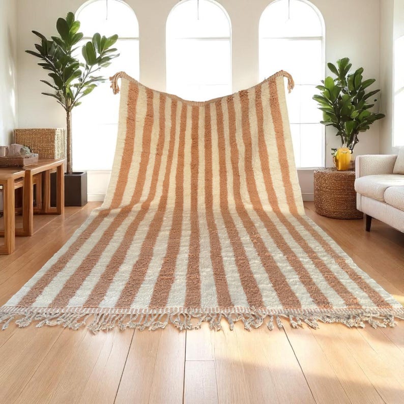Elegant handwoven Moroccan rug with vertical stripes in Cameo Rose and soft white. Perfect for boho, coastal, minimalist, or Japandi-inspired spaces. Made from natural wool, this artisan piece blends texture and comfort for your living room, bedroom, or entryway. A modern pastel rug with warm earthy tones and timeless Amazigh character. Custom sizes available.