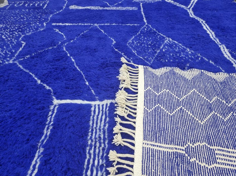 Striking handmade Moroccan rug in bold cobalt blue with white tribal Amazigh symbols. Crafted from natural wool, this unique Berber rug features traditional abstract lines and diamond motifs, perfect for adding a splash of color and culture to modern interiors. Ideal for boho, eclectic, or contemporary homes looking for a statement piece. Soft texture and timeless authenticity.