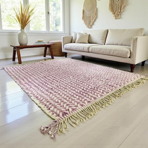 Handwoven Moroccan wool rug in wistful mauve and cream tones. Features a soft geometric pattern with textured pile and hand-knotted fringes. Perfect for living rooms, bedrooms, or boho interiors. Made from 100% natural wool by Berber artisans in Morocco. This handmade rug adds warmth, elegance, and Moroccan authenticity to modern or vintage-style spaces.