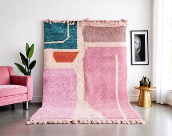 May include: A pink, orange, teal, and brown abstract geometric rug with white lines and fringe.