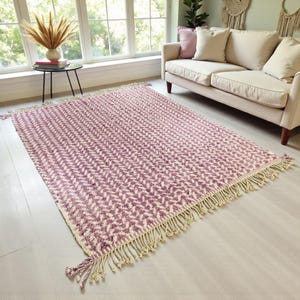 Handwoven Moroccan wool rug in wistful mauve and cream tones. Features a soft geometric pattern with textured pile and hand-knotted fringes. Perfect for living rooms, bedrooms, or boho interiors. Made from 100% natural wool by Berber artisans in Morocco. This handmade rug adds warmth, elegance, and Moroccan authenticity to modern or vintage-style spaces.