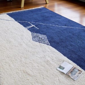 Handmade Moroccan wool rug in navy blue and ivory with a bold split design and fine geometric detailing. Handwoven by Berber artisans in Morocco using 100% natural wool, this rug is soft, eco-friendly, and durable. The modern minimalist design brings elegance and contrast to living rooms, bedrooms, or offices. Its clean color palette pairs effortlessly with neutral or bold interiors, making it a versatile statement piece. Finished with hand-knotted fringes for authenticity.