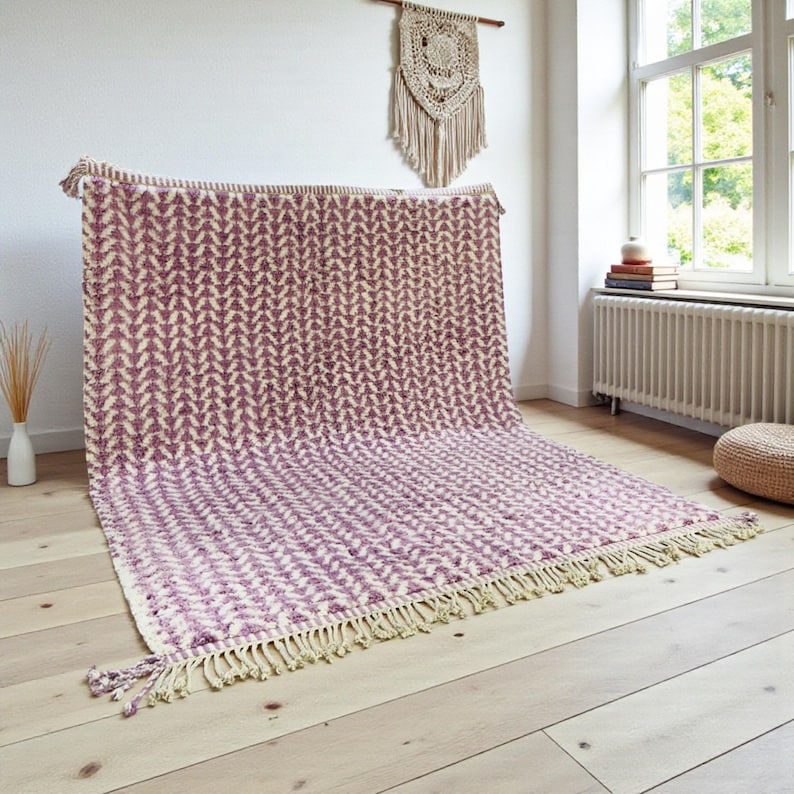 Handwoven Moroccan wool rug in wistful mauve and cream tones. Features a soft geometric pattern with textured pile and hand-knotted fringes. Perfect for living rooms, bedrooms, or boho interiors. Made from 100% natural wool by Berber artisans in Morocco. This handmade rug adds warmth, elegance, and Moroccan authenticity to modern or vintage-style spaces.