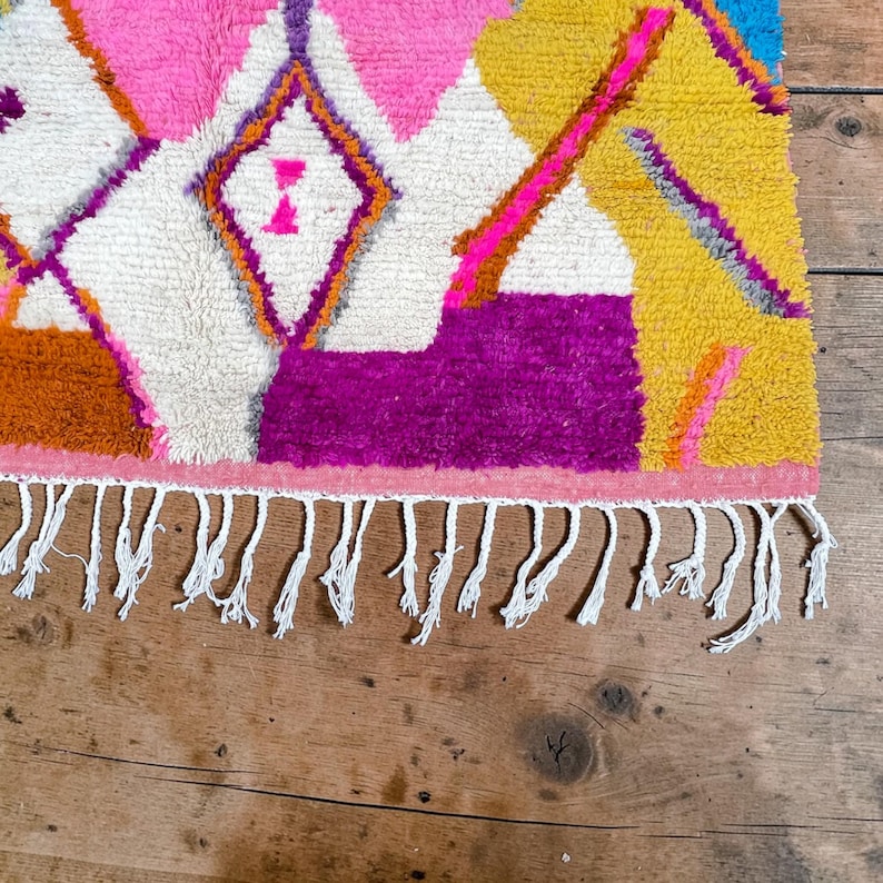 Authentic handmade Moroccan Boujaad rug featuring bold geometric diamond patterns in vibrant multicolor — electric blue, fuchsia pink, orange, yellow and purple on ivory wool background. Hand-knotted by Berber artisans in Morocco using natural wool. Perfect boho statement rug for living room, bedroom or dining room. One-of-a-kind colorful area rug with traditional fringe.