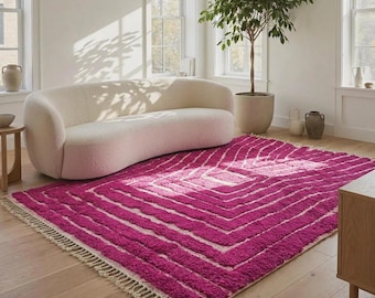 May include: A rectangular area rug featuring a vibrant magenta and cream geometric pattern of concentric squares. The rug has a thick, textured pile and is finished with cream-coloured fringe along the two shorter edges, lying flat on a floor.