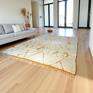Handmade Moroccan rug in a soft ivory base with striking mustard yellow (Thai Curry) abstract lines. Woven by Berber artisans in pure wool, this rug blends tradition and modern style. Its geometric tribal pattern and warm tones make it perfect for living rooms, bedrooms, or creative interiors. Durable, eco-friendly, and soft underfoot, this ivory and mustard Berber carpet adds Moroccan charm and luxury to boho, modern, or eclectic home decor.