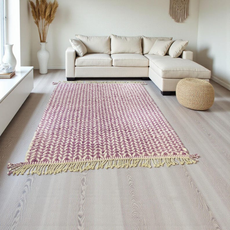 Handwoven Moroccan wool rug in wistful mauve and cream tones. Features a soft geometric pattern with textured pile and hand-knotted fringes. Perfect for living rooms, bedrooms, or boho interiors. Made from 100% natural wool by Berber artisans in Morocco. This handmade rug adds warmth, elegance, and Moroccan authenticity to modern or vintage-style spaces.