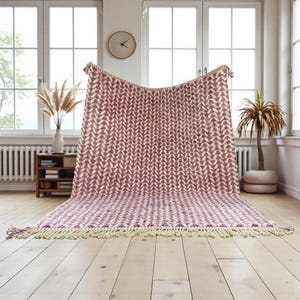 Handwoven Moroccan wool rug in wistful mauve and cream tones. Features a soft geometric pattern with textured pile and hand-knotted fringes. Perfect for living rooms, bedrooms, or boho interiors. Made from 100% natural wool by Berber artisans in Morocco. This handmade rug adds warmth, elegance, and Moroccan authenticity to modern or vintage-style spaces.