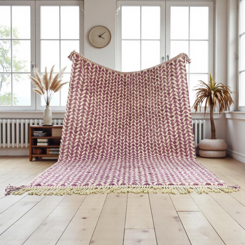 Handwoven Moroccan wool rug in wistful mauve and cream tones. Features a soft geometric pattern with textured pile and hand-knotted fringes. Perfect for living rooms, bedrooms, or boho interiors. Made from 100% natural wool by Berber artisans in Morocco. This handmade rug adds warmth, elegance, and Moroccan authenticity to modern or vintage-style spaces.
