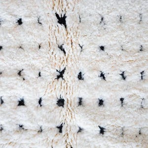 Handmade Moroccan rug in black and white with a dotted Berber pattern and bold black stripe edges. Crafted from natural wool by artisans in the Atlas Mountains, this rug combines authenticity and modern design. Perfect for boho chic, Scandinavian, and minimalist interiors, it brings warmth, texture, and elegance to living rooms, bedrooms, and creative spaces. A luxury Moroccan wool carpet that blends artisanal tradition with contemporary home decor style.