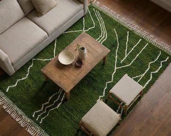 May include: A deep green area rug with a white linear pattern and fringed edges, positioned under a wooden coffee table, two light-coloured upholstered ottomans, and a light-coloured sofa on a dark wood floor with a bowl and vase on the table.