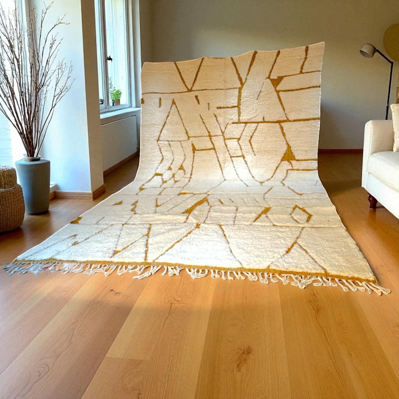Handmade Moroccan rug in a soft ivory base with striking mustard yellow (Thai Curry) abstract lines. Woven by Berber artisans in pure wool, this rug blends tradition and modern style. Its geometric tribal pattern and warm tones make it perfect for living rooms, bedrooms, or creative interiors. Durable, eco-friendly, and soft underfoot, this ivory and mustard Berber carpet adds Moroccan charm and luxury to boho, modern, or eclectic home decor.