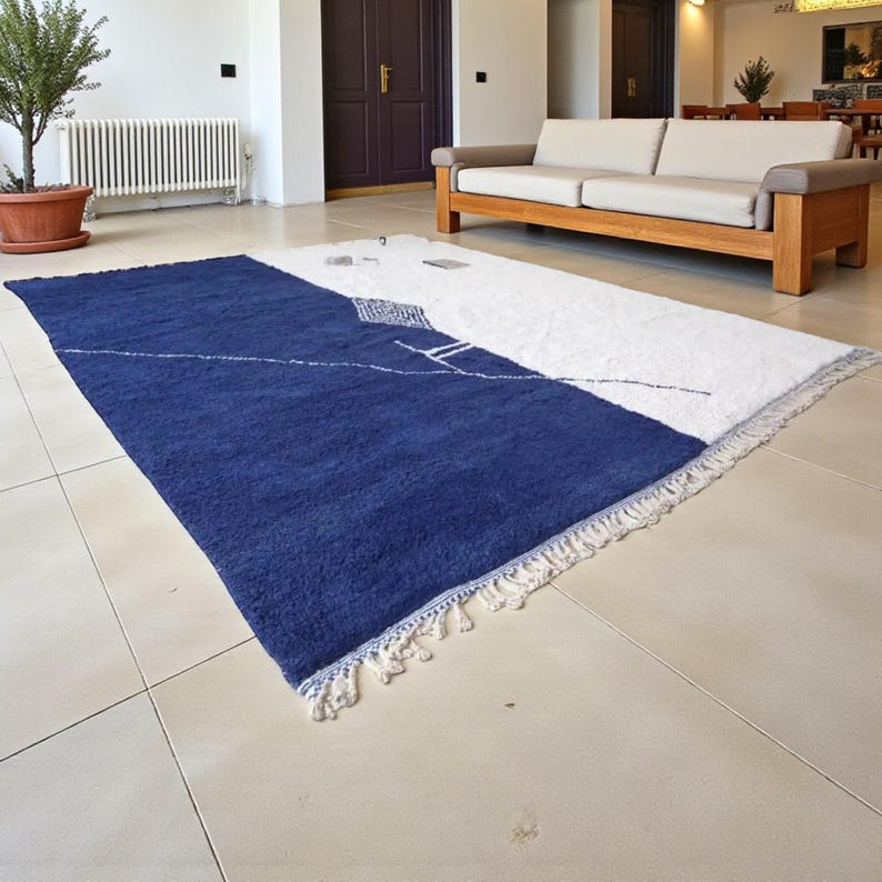 Handmade Moroccan wool rug in navy blue and ivory with a bold split design and fine geometric detailing. Handwoven by Berber artisans in Morocco using 100% natural wool, this rug is soft, eco-friendly, and durable. The modern minimalist design brings elegance and contrast to living rooms, bedrooms, or offices. Its clean color palette pairs effortlessly with neutral or bold interiors, making it a versatile statement piece. Finished with hand-knotted fringes for authenticity.