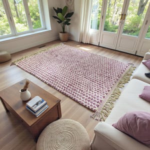 Handwoven Moroccan wool rug in wistful mauve and cream tones. Features a soft geometric pattern with textured pile and hand-knotted fringes. Perfect for living rooms, bedrooms, or boho interiors. Made from 100% natural wool by Berber artisans in Morocco. This handmade rug adds warmth, elegance, and Moroccan authenticity to modern or vintage-style spaces.