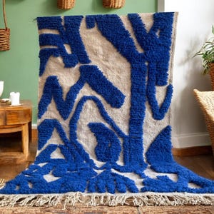 A vintage Moroccan wool rug with a bold blue abstract design handwoven on a neutral beige background, featuring plush texture and traditional fringed edges Vintage Rug, Moroccan Rug Wool Rug Abstract Rug Handwoven Rug Blue Rug Bold Design Modern Rug