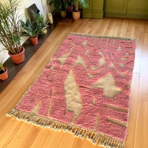Modern abstract Moroccan Beni Mrirt rug featuring soft pink and beige tones with artistic organic patterns. Handwoven with premium wool by Amazigh artisans in Morocco. This boho-chic rug is perfect for adding an artistic touch to contemporary, minimalist, or eclectic interiors. Plush and cozy underfoot, it’s ideal for living rooms, bedrooms, and stylish creative spaces. Unique handmade piece crafted with passion and heritage.