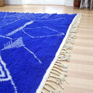 Striking handmade Moroccan rug in bold cobalt blue with white tribal Amazigh symbols. Crafted from natural wool, this unique Berber rug features traditional abstract lines and diamond motifs, perfect for adding a splash of color and culture to modern interiors. Ideal for boho, eclectic, or contemporary homes looking for a statement piece. Soft texture and timeless authenticity.