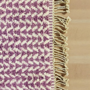 Handwoven Moroccan wool rug in wistful mauve and cream tones. Features a soft geometric pattern with textured pile and hand-knotted fringes. Perfect for living rooms, bedrooms, or boho interiors. Made from 100% natural wool by Berber artisans in Morocco. This handmade rug adds warmth, elegance, and Moroccan authenticity to modern or vintage-style spaces.
