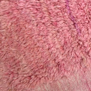 Handwoven Moroccan wool area rug in soft solid pink with a plush, high-pile texture and natural cream wool fringes. Made by Amazigh artisans in the Atlas Mountains, this minimalist Beni Ourain-style rug brings warmth, softness, and authentic Moroccan craftsmanship to modern boho or minimalist interiors.