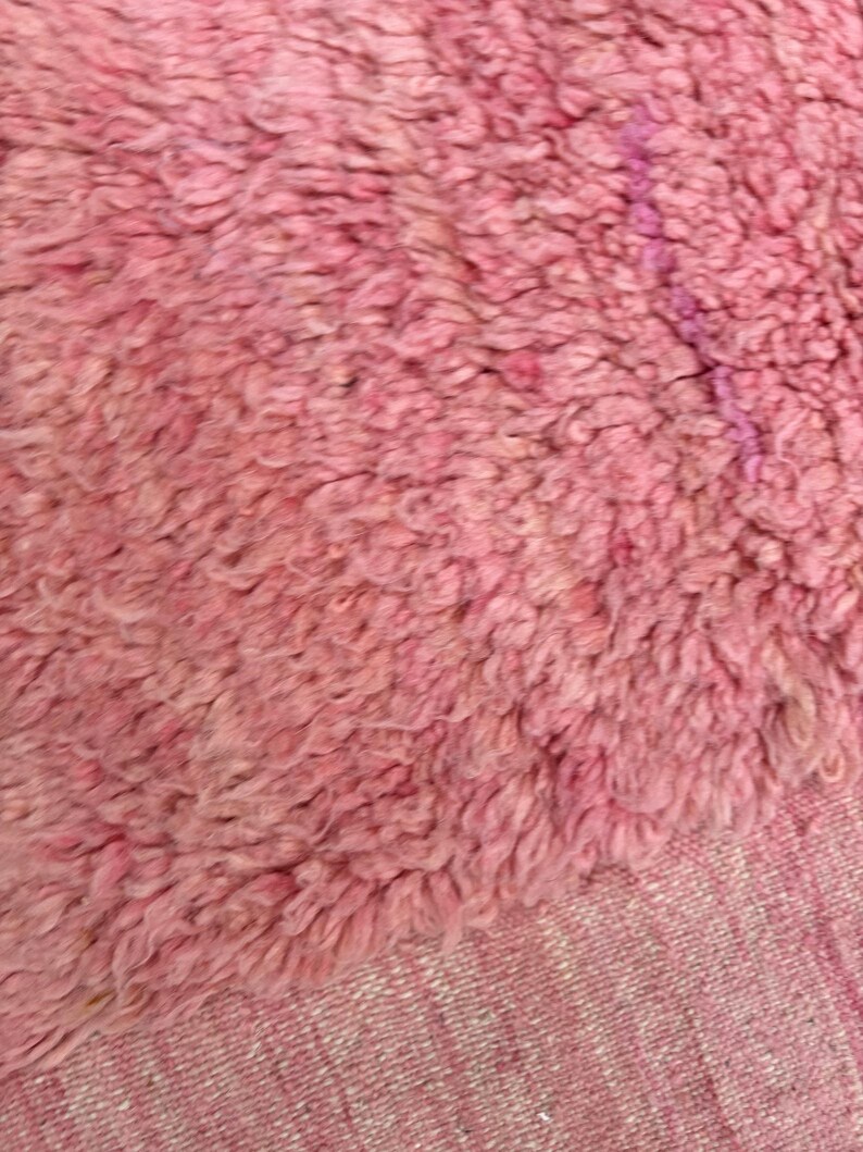 Handwoven Moroccan wool area rug in soft solid pink with a plush, high-pile texture and natural cream wool fringes. Made by Amazigh artisans in the Atlas Mountains, this minimalist Beni Ourain-style rug brings warmth, softness, and authentic Moroccan craftsmanship to modern boho or minimalist interiors.