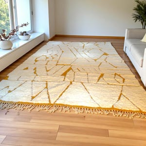 Handmade Moroccan rug in a soft ivory base with striking mustard yellow (Thai Curry) abstract lines. Woven by Berber artisans in pure wool, this rug blends tradition and modern style. Its geometric tribal pattern and warm tones make it perfect for living rooms, bedrooms, or creative interiors. Durable, eco-friendly, and soft underfoot, this ivory and mustard Berber carpet adds Moroccan charm and luxury to boho, modern, or eclectic home decor.