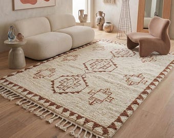 Può includere: Un tappeto rettangolare con base color crema e un motivo geometrico ripetuto in marrone. Il tappeto presenta un pelo spesso e strutturato ed è rifinito con lunghe frange annodate lungo i bordi più corti dell'articolo.