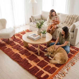 May include: A living room scene featuring a geometric patterned rug in shades of rust and orange. A round wooden coffee table sits in the center, with a beige sofa and armchair. A golden retriever dog is lying on the rug.