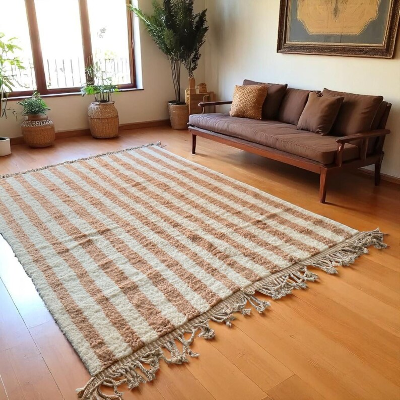 Elegant handwoven Moroccan rug with vertical stripes in Cameo Rose and soft white. Perfect for boho, coastal, minimalist, or Japandi-inspired spaces. Made from natural wool, this artisan piece blends texture and comfort for your living room, bedroom, or entryway. A modern pastel rug with warm earthy tones and timeless Amazigh character. Custom sizes available.