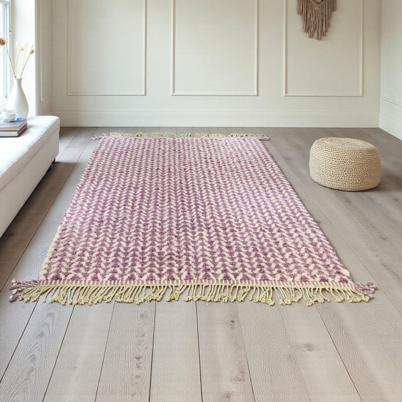 Handwoven Moroccan wool rug in wistful mauve and cream tones. Features a soft geometric pattern with textured pile and hand-knotted fringes. Perfect for living rooms, bedrooms, or boho interiors. Made from 100% natural wool by Berber artisans in Morocco. This handmade rug adds warmth, elegance, and Moroccan authenticity to modern or vintage-style spaces.