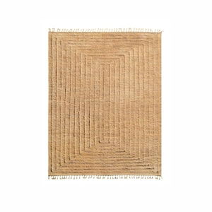 Puede incluir: Una alfombra rectangular de color marrón claro con un patrón geométrico de líneas tejidas. La alfombra tiene un borde de flecos.