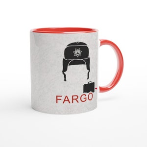 Könnte beinhalten: Weiße Keramiktasse mit rotem Innenraum und Griff. Die Tasse zeigt eine schwarze Grafik eines Hutes, Haares und einer Aktentasche mit dem Wort "FARGO" in Rot. Die Tasse hat einen strukturierten, cremefarbenen Hintergrund.