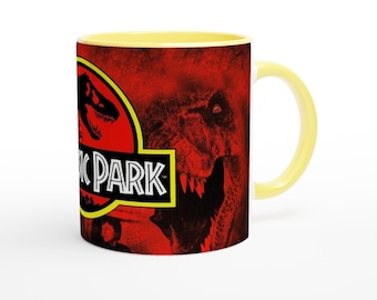 May include: A white ceramic mug with a yellow rim. The mug features a red and black graphic of a dinosaur from the movie Jurassic Park. The text "Jurassic Park" is printed in black and yellow on the mug.