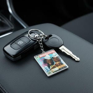 May include: A keychain featuring a rectangular charm with a Nickelodeon "Good Burger" design. The charm is attached to a silver keyring with a car key and a remote key fob. The items are on a black leather surface.