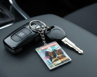 May include: A keychain featuring a rectangular charm with a Nickelodeon "Good Burger" design. The charm is attached to a silver keyring with a car key and a remote key fob. The items are on a black leather surface.
