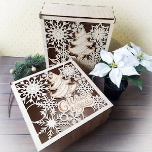 May include: Two wooden boxes with intricate snowflake and Christmas tree designs. The boxes are made of light wood and have a cutout design. The larger box has the text "С Новым Годом" which translates to "Happy New Year" in English.