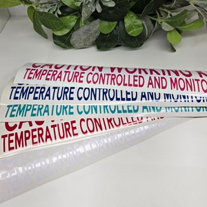 Puede incluir: Cinco pegatinas blancas con el texto "CAUTION WORKING AREA TEMPERATURE CONTROLLED AND MONITORED" en diferentes colores: rojo, azul marino, verde azulado, rojo y blanco.